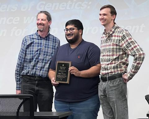 The image shows Shawn Thomas holding a plaque and standing between Jacob Washburn and David Braun